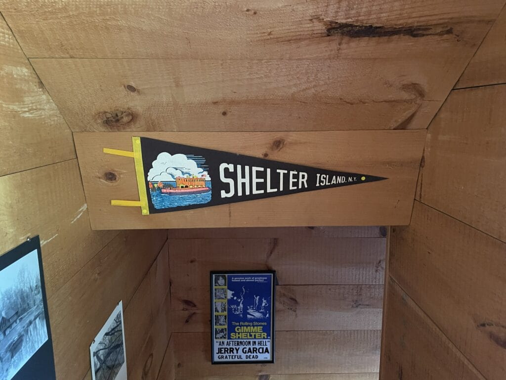 Vintage black pennant reading 'Shelter Island' with yellow tabs and a small seaside illustration on a wooden wall.